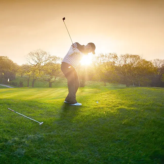 Golfer teeing off at sunrise